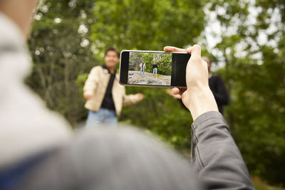 Copped image of teenage boy photographing friends dancing at park