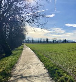 Empty road amidst field against sky