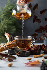 Woman pours fresh tea into cup on table with ingredients