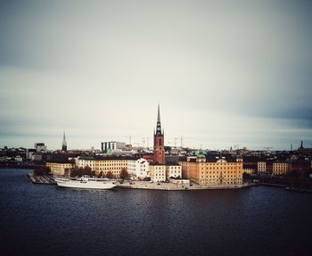 Buildings at waterfront against cloudy sky