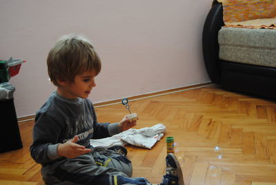 Cute boy blowing bubbles while sitting on hardwood floor at home