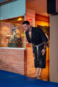 Karate man posing with a bow to access on tatami wearing black kimono