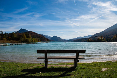 Bench by lake against sky