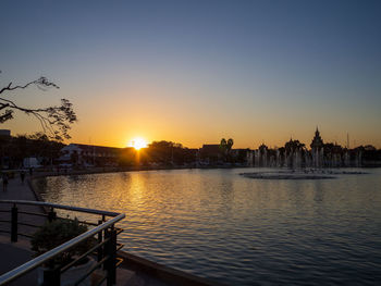 Scenic view of river by buildings against sky during sunset