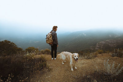 Man with dog standing on mountain against sky