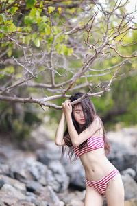 Sensuous young woman wearing bikini standing by tree