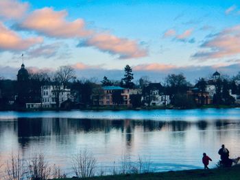 People on lake by buildings against sky during sunset