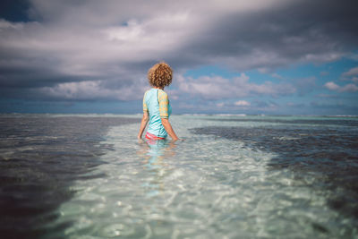 Side view of woman standing in sea against cloudy sky