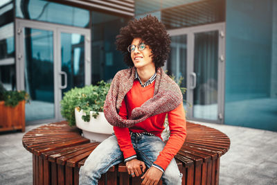 Thoughtful young man sitting on wooden bench in city