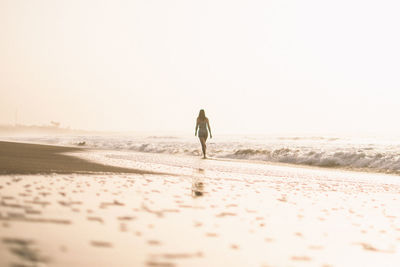 Rear view of man walking on beach against clear sky