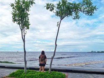 Rear view of woman standing by sea against sky