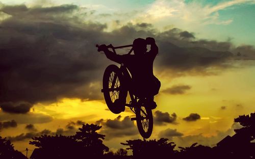 Silhouette boy performing stunt against sky during sunset