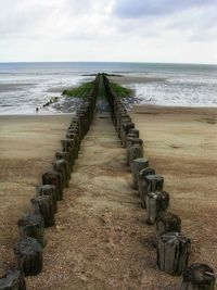 Wooden posts on beach against sky