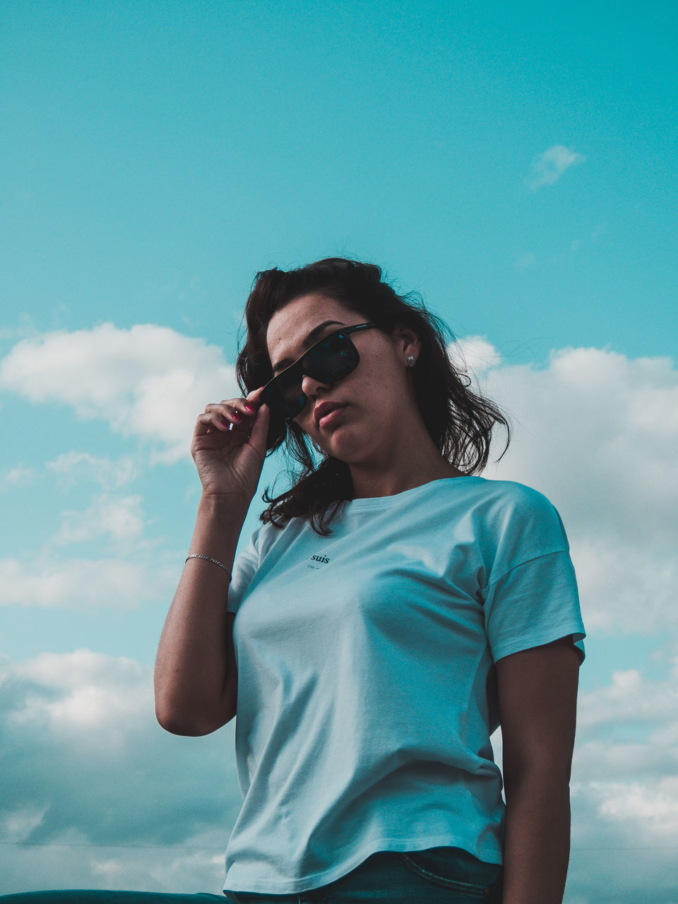 LOW ANGLE VIEW OF YOUNG WOMAN HOLDING BLUE SKY AGAINST CLOUDS
