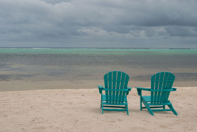 Empty chairs on beach against sky