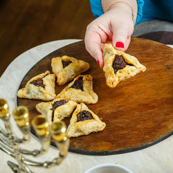 Women's hands laying gomentashi cookies on a wooden board for the festive table for purim.