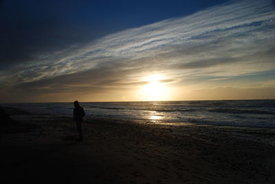 Silhouette man walking on beach against sky during sunset