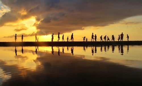 Silhouette people on beach against sky during sunset