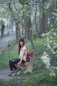 Full length of woman sitting on seat by trees at park