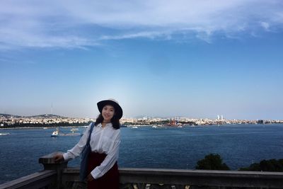 Portrait of young woman sitting against sea and cityscape