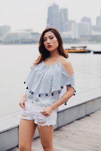 Portrait of beautiful young woman standing against water