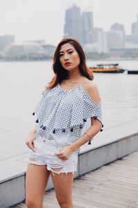 Portrait of young woman standing against river in city