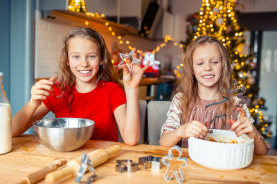 Portrait of smiling girl with sister making christmas cookies at home