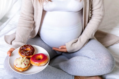 Midsection of pregnant woman having donuts on bed at home