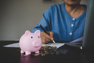 Midsection of woman inserting coin in piggy bank