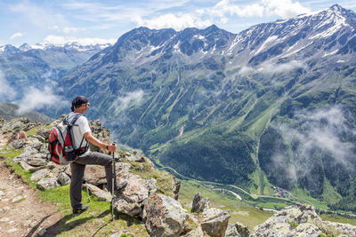 Rear view of man sitting on rock against mountains