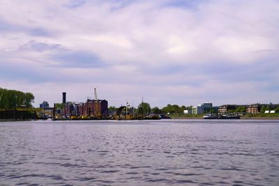 View of buildings by river against cloudy sky
