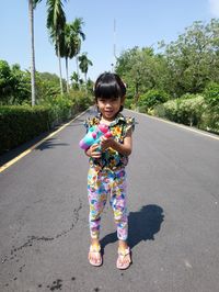 Portrait of cute girl standing on road against trees