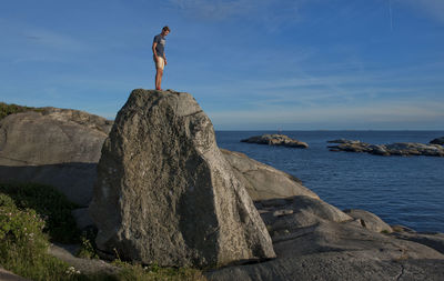 Man standing on rock by sea against sky