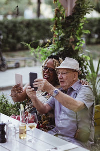 Cheerful senior couple taking selfie on smart phone while sitting in sidewalk cafe