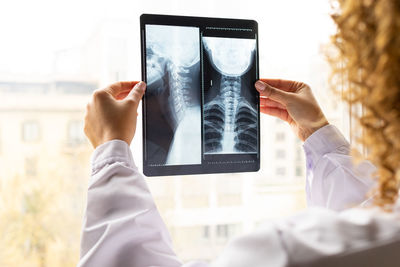 Anonymous ethnic female medic in uniform studying x ray image of spine on window in office