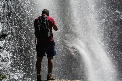 Rear view of man standing against waterfall