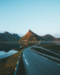 Road leading towards mountains against clear sky