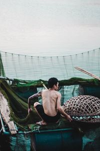 Rear view of shirtless man sitting in basket against sky