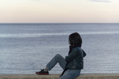 Rear view of woman looking at sea against sky during sunset