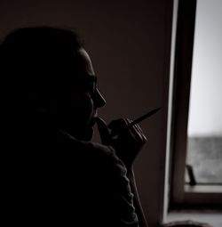 Side view of man looking through window at home