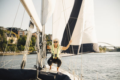 Senior woman crouching while holding rope in boat on sunny day