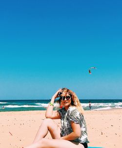Woman wearing sunglasses on beach against clear blue sky