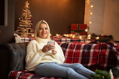 Portrait of smiling young woman using mobile phone while sitting on sofa at home