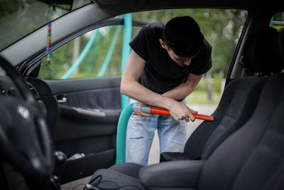 Caucasian man vacuuming a car at a gas station.