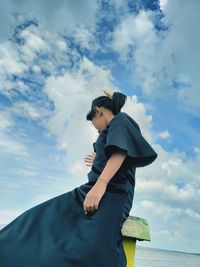 Low angle view of girl sitting against sky