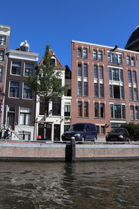 Canal by buildings against clear blue sky