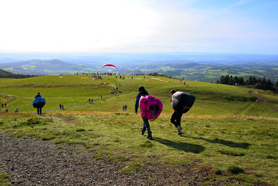 Rear view of people walking on field against sky