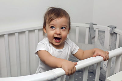 One year old child in white clothes standing in a white round bed in his nursery