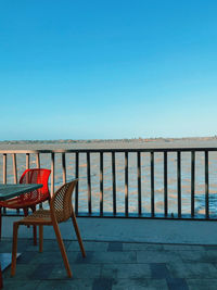 Empty chairs by railing against clear blue sky