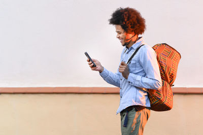 Young woman using mobile phone against wall